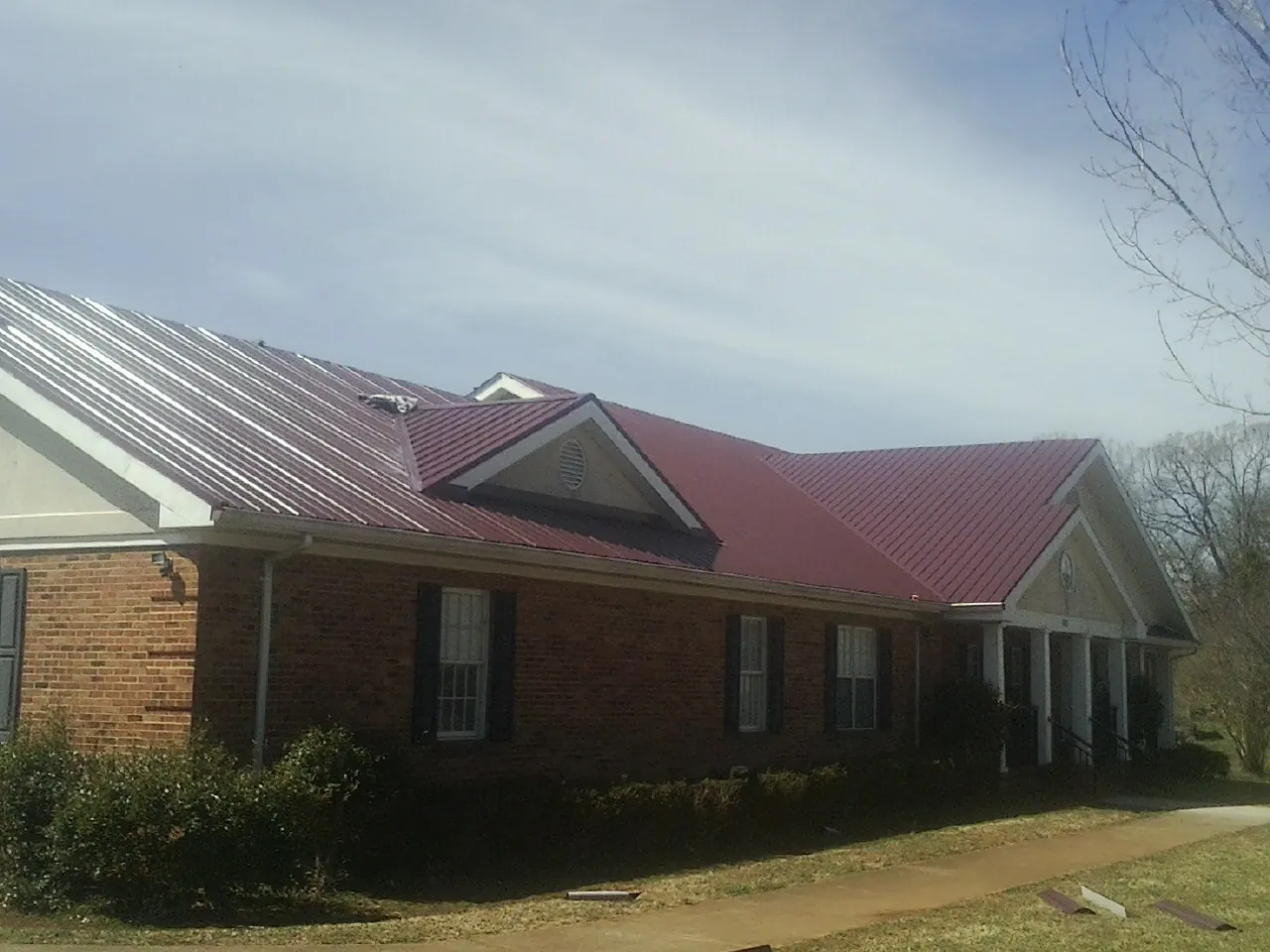 Red metal roof with gabled entries on a long brick building, from a Hail Damage Roof Repair job in Pleasant Prairie