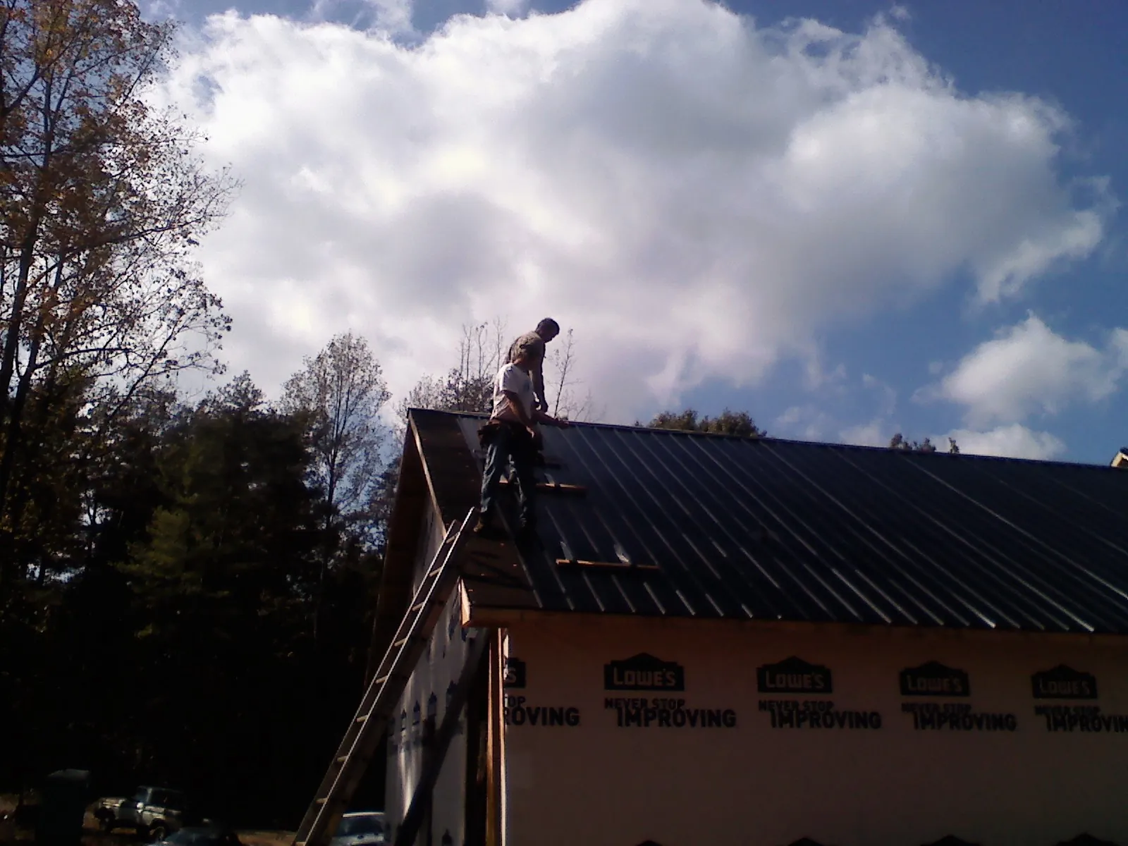 Roofer fastening dark metal panels high against a cloudy sky, from a Roof Inspection job in Pleasant Prairie