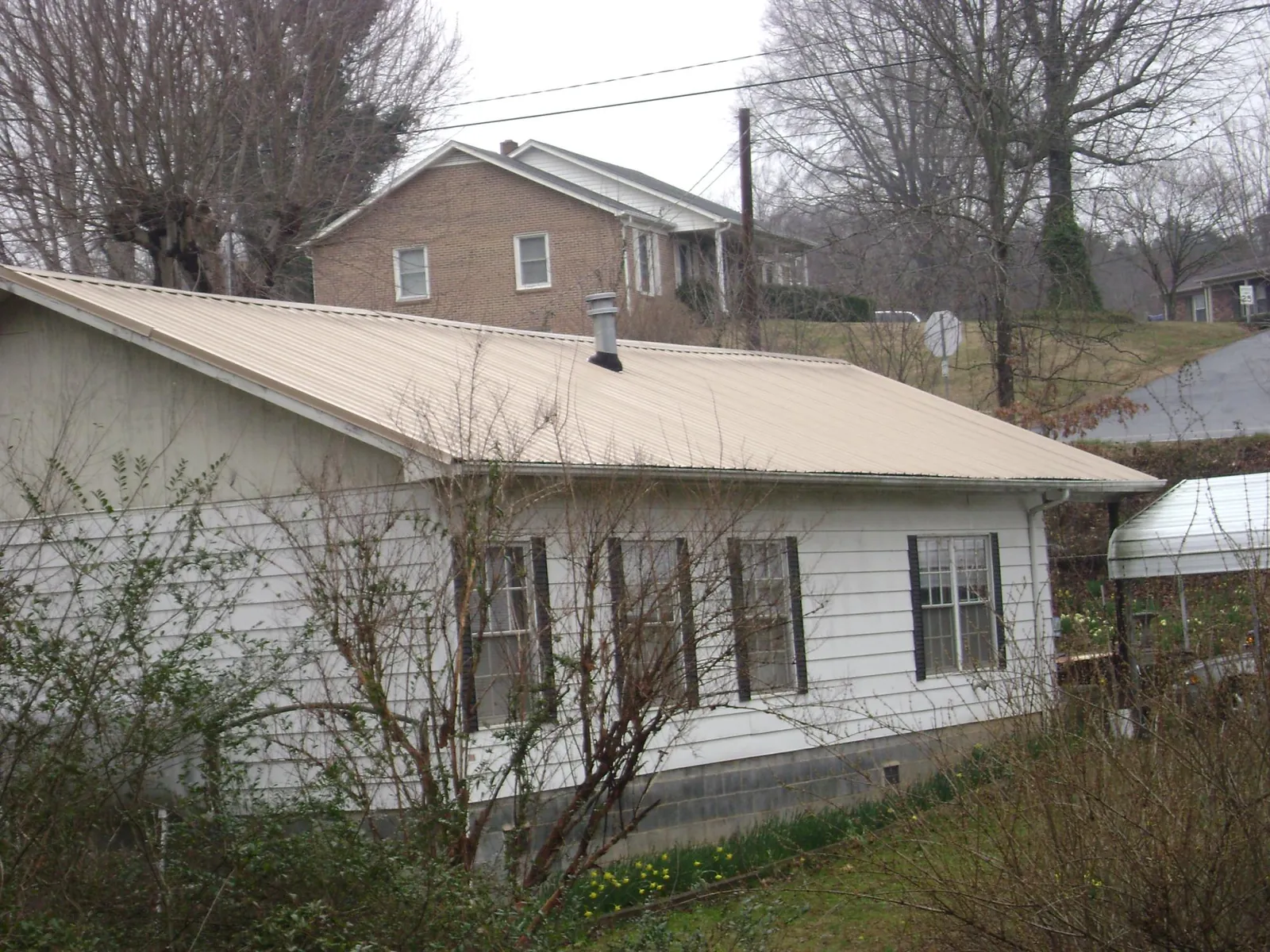 Tan metal roof on a white sided house set into a hillside — Commercial Roofing by Roofing Brothers in Pleasant Prairie